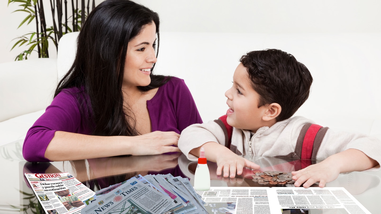 Mama´y y niño frente a frente sonriendo y apuntando hacia las manualidades sobre la mesa